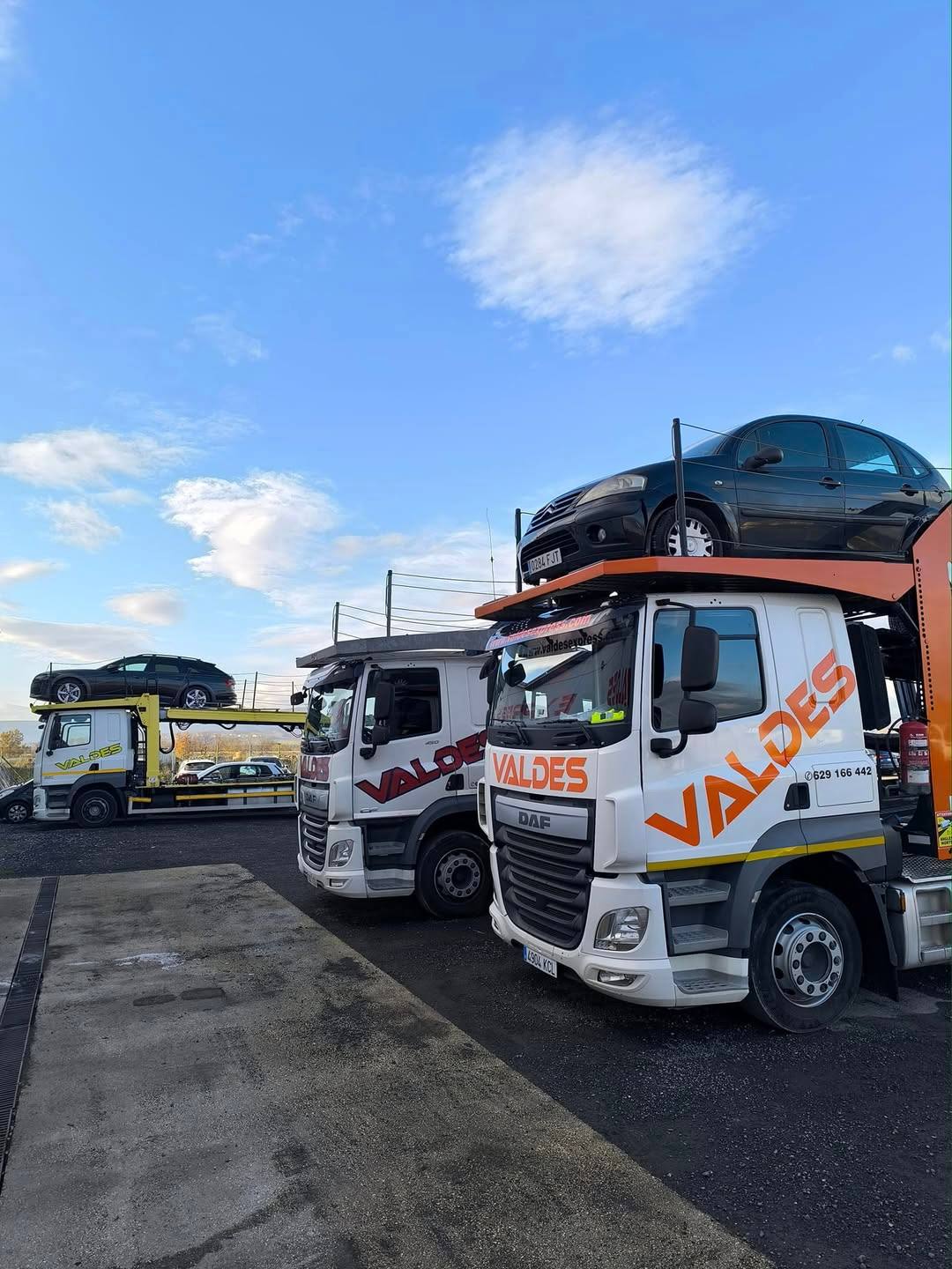 Camiones portavehículos de Valdés Express aparcados, el primero cargado con un coche en el piso de arriba