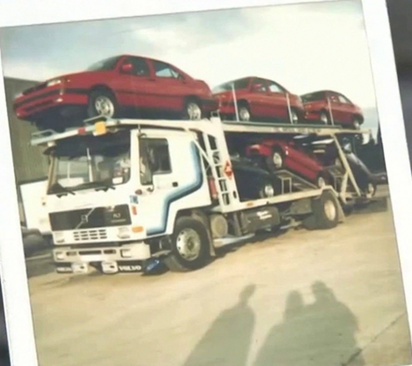 Foto antigua de un camión portacoches Volvo cargado de coches rojos